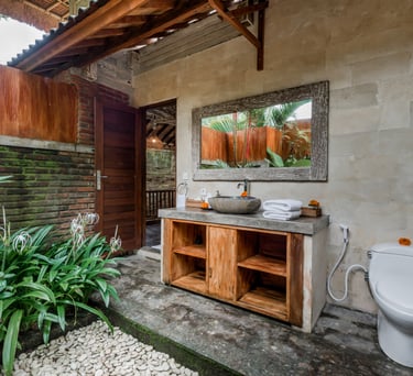 Rustic tropical outdoor bathroom with stone vessel sink, wooden vanity, and white toilet.