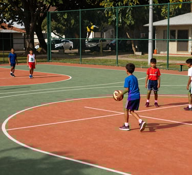 An outdoor multi-sports court with soft green fences, vibrant orange markings, and young children in sports gear, South American setting.