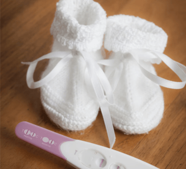 Positive pregnancy test result next to white knitted baby booties on a wooden background.