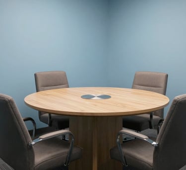 A private, professional consultation room in a North American / US office. A round table sits in the center with comfortable chairs. The walls are a calming Light Blue, suggesting a trustworthy and safe space for legal discussions.