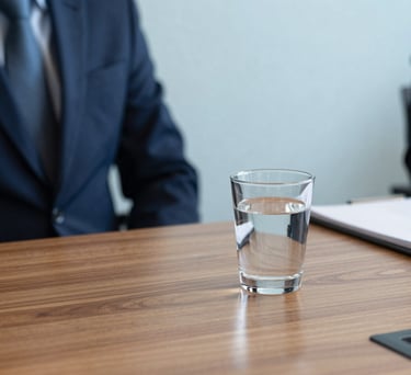 A close-up photograph of a professional meeting table in a Danish office, featuring high-quality wooden surfaces, a glass of water, and a notepad, with soft morning light and a color palette of deep navy blue and pale sky blue.