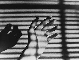 A black and white image of a man's hand with blinds casting shadow.