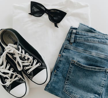 A white T-shirt, blue jeans, black sunglasses, and black sneakers with white shoelaces