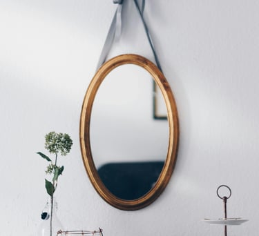 A gold mirror hanging on the wall above some decor on a wood table