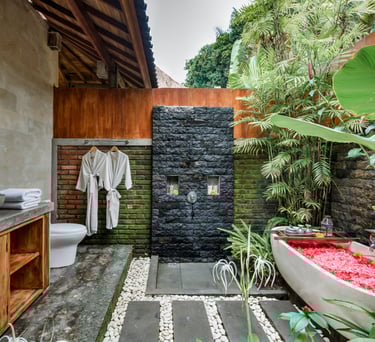 Luxury outdoor bathroom in Bali featuring a stone shower and a bathtub filled with red flower petals.