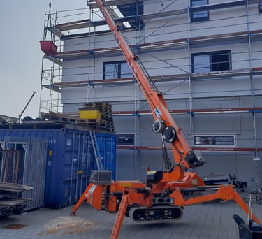 Oranger Kran "Jekko SPD360" auf Baustelle vor eingerüstetem Mehrfamilienhaus.