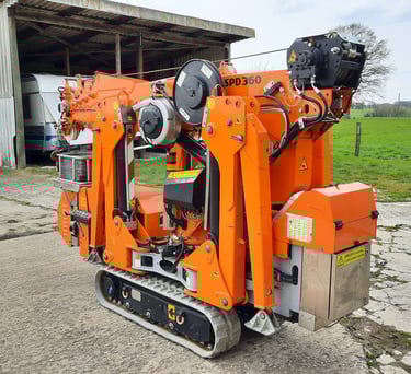 Kompakter oranger Minikran SPD360 auf Raupenketten, zusammengefaltet vor einer Scheune.