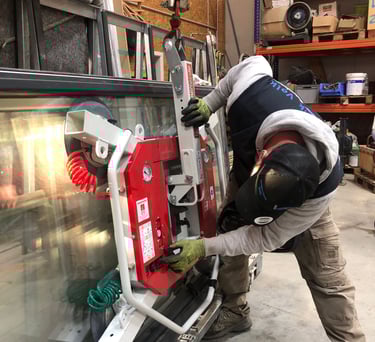 Schreinermeister Ferdinand Volk justiert den roten Vakuum-Saugheber an einer großen Glasscheibe, die an einem Kranhaken ist.