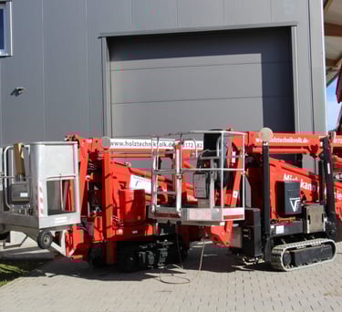 Zwei rote Raupen-Arbeitsbühnen mit silbernen Körben stehen nebeneinander vor einer grauen Industriehalle der Schreinerei Volk