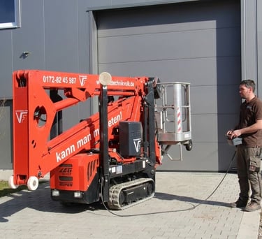 Schreinermeister Ferdinand Volk steuert die rote Raupen-Arbeitsbühne per Kabelfernbedienung vor seiner Werkhalle am Ammersee.