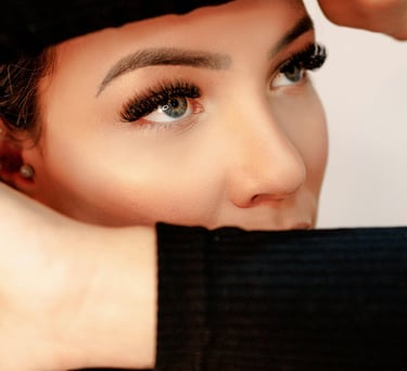 Primer plano de una mujer con extensiones de pestañas largas y cejas delineadas posando con sus mano