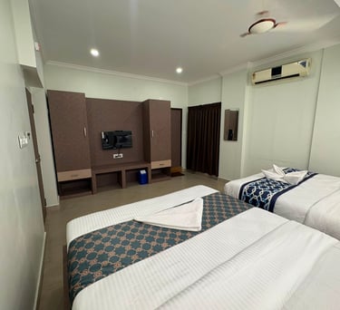 Modern hotel double room featuring twin beds with patterned runners and a wooden wall unit with television.