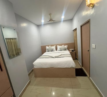Modern minimalist hotel bedroom with a white double bed, wood headboard, and wall-mounted mirror.