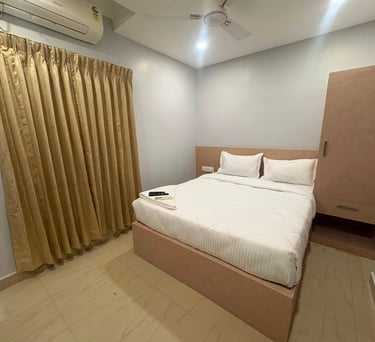 Modern minimalist hotel bedroom with white linens, gold curtains, and a wooden wardrobe cabinet.
