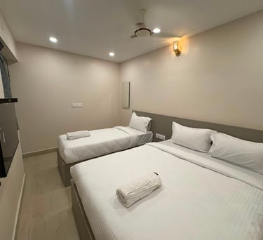 Modern hotel room featuring a twin bed and queen bed with white linens and a wall-mounted TV.