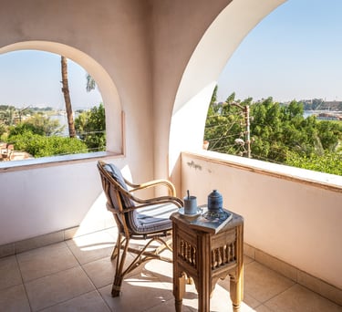 Sunny Nile view balcony with a wicker chair and side table overlooking the Nile River in Egypt.
