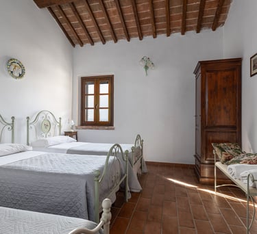 Rustic Italian bedroom with twin iron beds, terracotta tile floors, and wooden beamed ceilings.