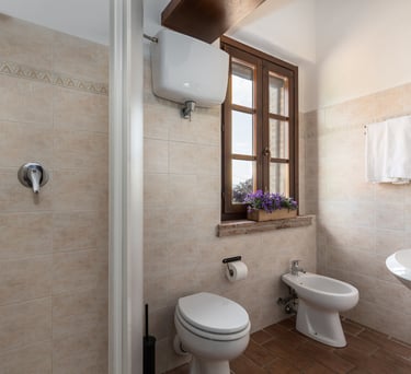 Modern rustic bathroom featuring beige tiles, walk-in shower, white bidet, and a wooden window.