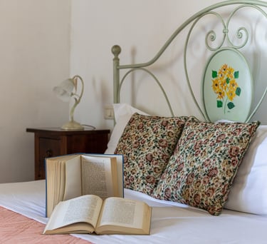 Cozy bedroom with open books on a bed featuring floral pillows and a vintage metal headboard.
