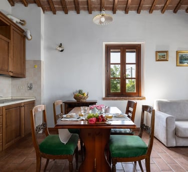 Rustic open plan kitchen and dining area with wooden table, green chairs, and exposed ceiling beams.