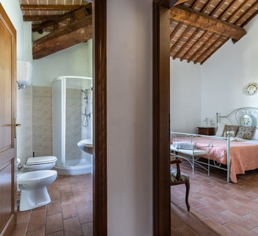 Rustic Italian bedroom and ensuite bathroom with terracotta tile floors and exposed wood beam ceilings.