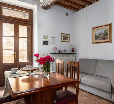 Rustic Italian dining room with a wooden table, gray sofa, and balcony doors.