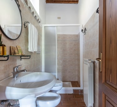 Modern rustic bathroom interior with white ceramic sink, bidet, and glass walk-in shower stall.