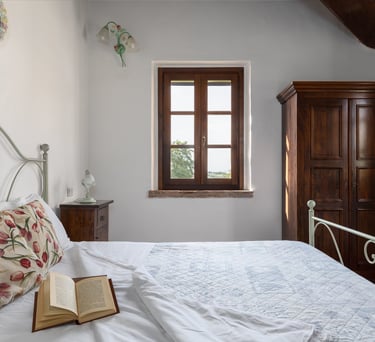 Rustic bedroom with a white iron bed frame, floral pillows, an open book, and a vintage wooden wardrobe.