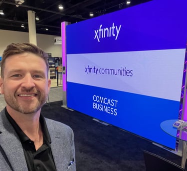 Chris takes a selfie in front of a blue Xfinity Comcast Business booth at a professional trade show.