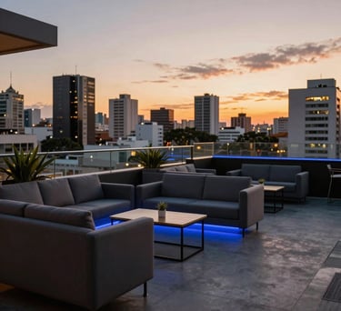 An outdoor corporate lounge at sunset in a South American city, featuring comfortable modern seating, ambient blue lighting, and a view of urban architecture.