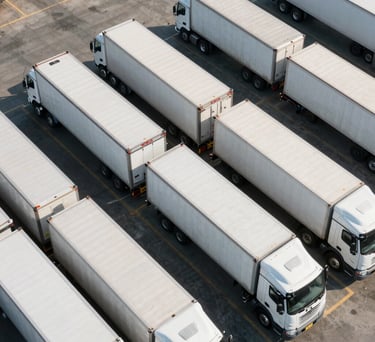 An aerial view of a clean, organized logistics yard in North America with white semi-trailers precisely lined up. Morning sunlight casting soft shadows on the pavement.