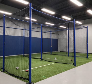 A wide-angle shot of professional indoor batting cages in North American / US, featuring steel blue netting and bright, modern white lighting.