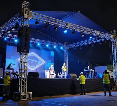 Cinematic shot of a stage being set up for a major event in Brazil, workers positioning steel structures under dramatic blue lighting.