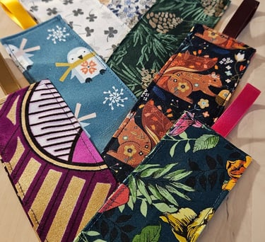 Handmade fabric bookmarks with colorful floral, animal, and geometric patterns and ribbon loops.