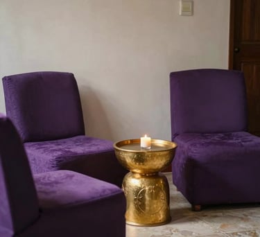 A comfortable seating area for clients in a South American spiritual center. Plush purple chairs, a golden side table, and a feeling of privacy and safety.