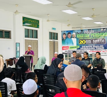 A man speaking at a podium during a community event at Dewan Masjid Seberang Takir.