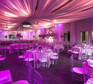Salón de eventos elegante con pista iluminada, mesas decoradas y luces colgantes.