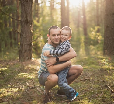 Šeimos fotosesijos akimirka - tėtis ir sūnus miško fone apsikabinę
