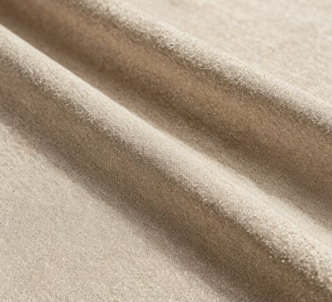 Close-up photography of a high-end textured linen fabric in soft beige tones, natural sunlight creating subtle shadows, editorial style, Spanish-speaking aesthetic.