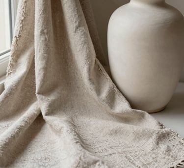 Close-up of a high-end textured linen fabric and a smooth off-white ceramic vase, soft natural lighting from a side window, Spanish-speaking studio setting, calm and airy composition.