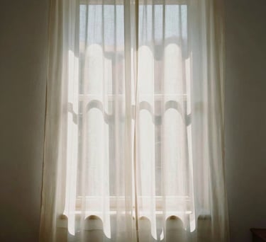 Abstract shot of sunlight through a sheer curtain in a Spanish-speaking interior, creating soft patterns on an off-white wall, evoking serenity and light.