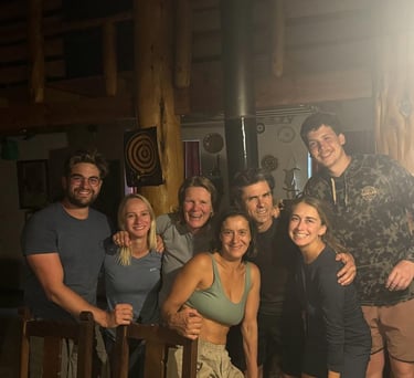 A group of seven people posing for a photo inside a wooden cabin.