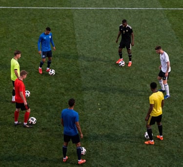 Wide shot of a soccer drill involving six players of diverse origins passing the ball in a triangular pattern. High-angle perspective, evening lighting.