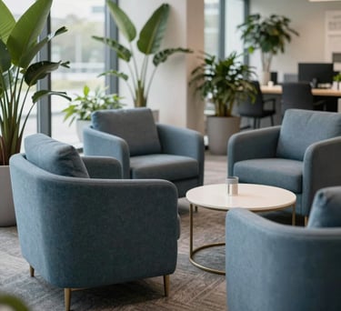 A bright collaboration zone with comfortable lounge chairs in slate blue, surrounded by indoor plants and natural light in a US corporate setting.