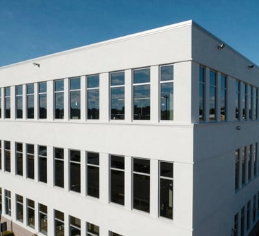 A high-angle architectural shot of a modern research facility with clean white lines and large windows reflecting a deep blue sky. North American / International style.