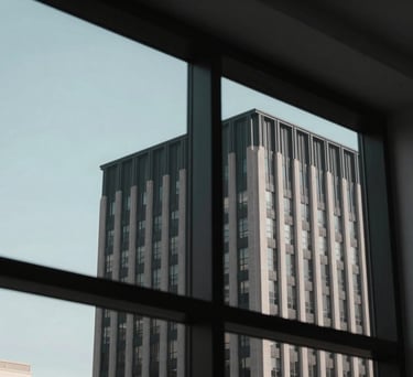 A view through a modern window in a North American / US city, showing the clean lines of professional architecture with a charcoal black and muted light blue sky background.