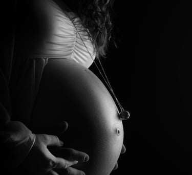 Black and white maternity photography profile of a pregnant woman's belly with hands and necklace.