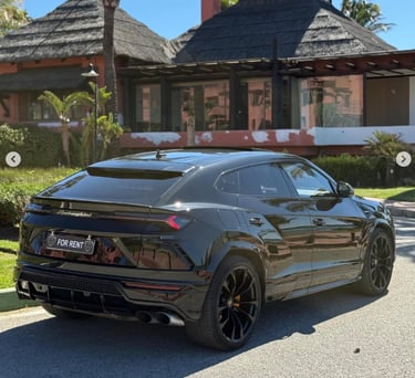 Luxury black Lamborghini Urus SUV for rent parked in front of a tropical resort villa.