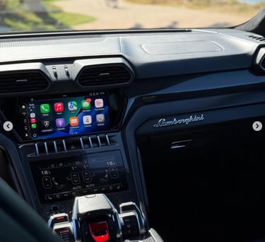 Interior view of a luxury Lamborghini Urus dashboard featuring Apple CarPlay and carbon fiber trim.