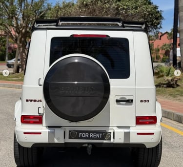 White Brabus 800 luxury SUV for rent parked on a sunny street with carbon fiber spare tire cover.